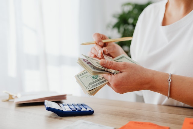 person counting a stack of American cash and with a notebook and calculator next to them